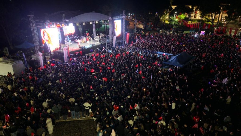 Bir konser alanında büyük bir kalabalık, sahnedeki sanatçıyı izliyor.
