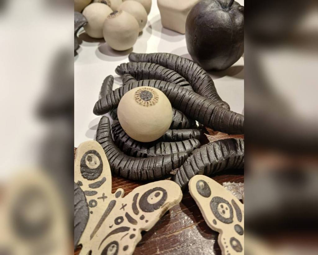 Kahverengi bir zemin üzerinde çeşitli şekillerde seramik objeler; siyah yuvarlak parçalar ve spiral şeklinde olanlar, üzerinde desenler olan iki kelebek figürü.